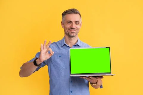 Smiling man presenting computer showing ok gesture on yellow background, copy 스톡 사진
