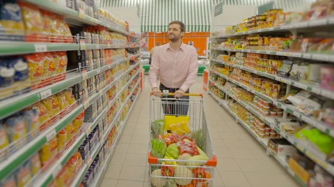 Smiling man pushing trolley and buy food at supermatket Stock Footage 63370734