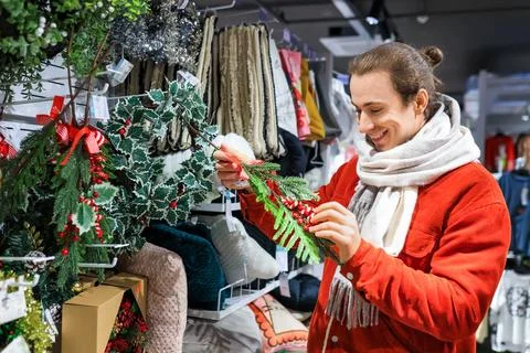 Smiling man in a red jacket and scarf choosing Christmas decorations in a s.. Stock Photos