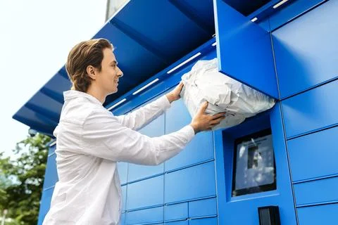 Smiling man retrieving a package from a blue parcel locker. Fast ecommerce .. Stockfoto's