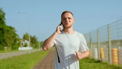 Smiling man runner speaking use phone feel happy outdoors at sunlight on street Stock Footage 140365867