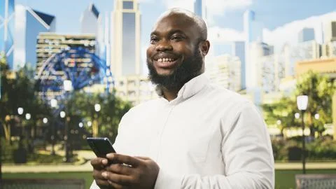 Smiling man scrolling mobile phone and looking toward camera Stock Photos