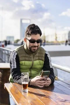 A smiling man sending messages while smiling at a bar near the river Stock Photos