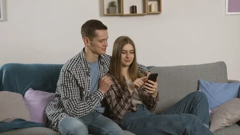 Smiling man showing thumb up while girlfriend using smartphone Vidéo 124950994