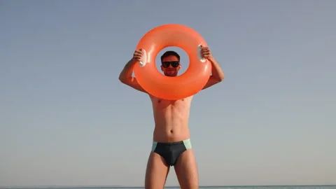 Smiling man shows and twirls beach inflatable ring in hands against sky. Stock Footage 271058751