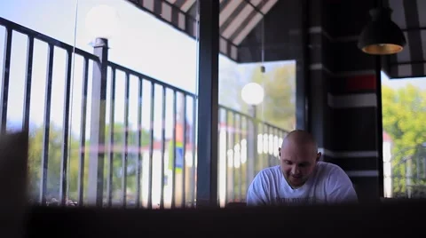 Smiling Man Sitting in a Cafe and Writes Something Occasionally Looking Out the Stock Footage 66690035