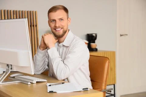 Smiling man sitting at desk with computer in modern office Stock Photos