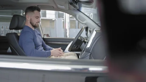 Smiling man sitting in new black car and enjoying car interior in auto salon. Stock Footage 101115887