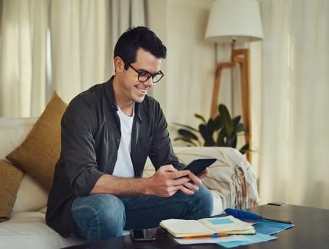 Smiling man sitting on sofa using digital tablet at home Stock Photos