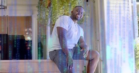Smiling man sitting on wooden bench at entry, wearing henley, shorts, necklace, Stock Photos
