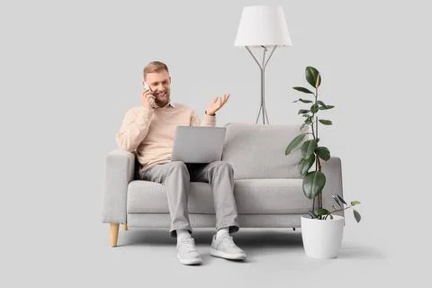 Smiling man on sofa talking on phone with laptop, remote work and communicati Stock Photos