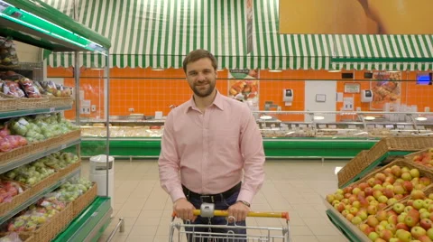 Smiling man standing with his trolley on aisle at supermarket Stock Footage 63431365