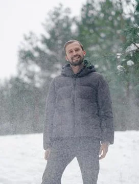 Smiling man standing under falling snow in winter pine forest Stock Photos