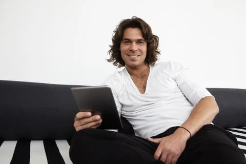 Smiling man with a tablet on a sofa Stock Photos