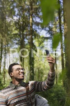 Smiling man taking selfie with camera phone in sunny woods Stock Photos