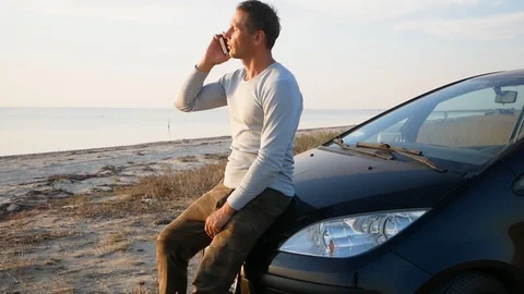 Smiling man talking on cell phone beside his car on a beach. Stock Footage 116161645