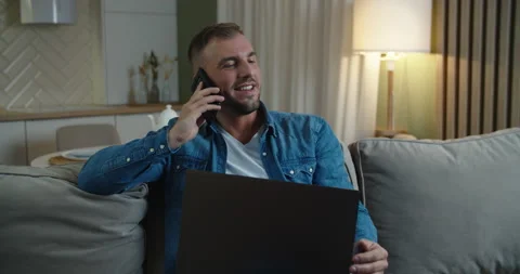 Smiling man talking on mobile phone, in his hands a laptop. Kitchen background Stock Footage 148132805