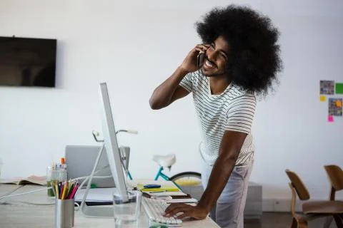 Smiling man talking on phone while using computer in office Stock Photos