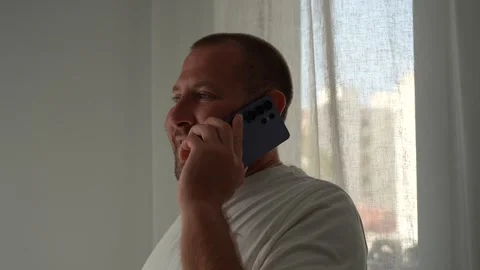 Smiling Man Talking on Smartphone Near Window at Home Stock Footage 341293214