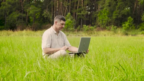 Smiling man talking on video online sitting on the lawn in the Grass Stock Footage 135825560