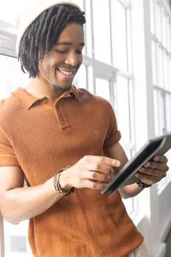 Smiling man tapping dark tablet near tall multi-pane windows, wearing Stock Photos