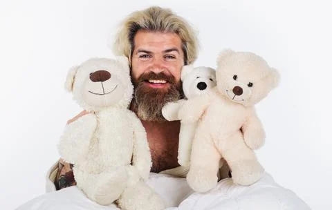 Smiling man with teddy bears in bed. Bearded guy with plush toys. Good mornin Stock Photos