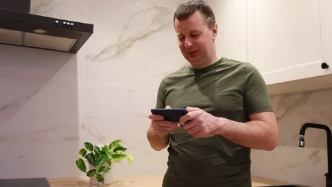Smiling Man Texting on Smartphone in Modern Kitchen During Evening Hours Stock Footage 273591010