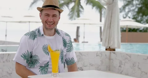 Smiling man tropical shirt drinking cocktail beachside resort, palm Видео 314044597