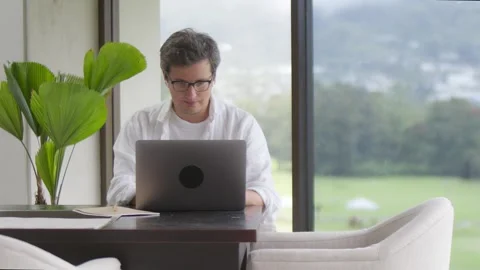 Smiling man typing in laptop sitting near panoramic window Stock-Footage 251362866
