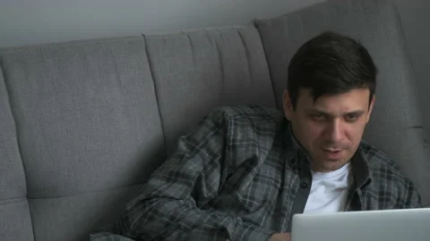 Smiling man is typing a message on laptop lying on sofa at home, working. Stock Footage 152970855