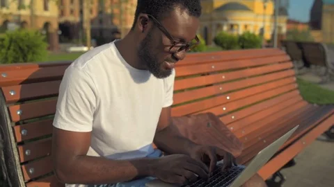Smiling man typing while working on a laptop in park Stock Footage 77810159