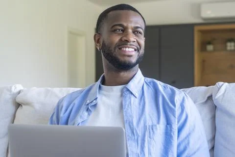 Smiling man using laptop at home on a bright couch, enjoying remote work an.. Stock Photos