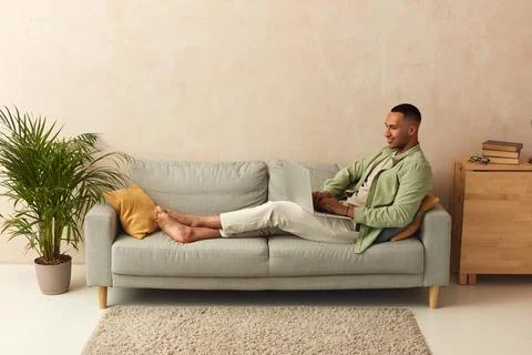 Smiling Man Using Laptop At Sofa. Guy Relaxing With Laptop At Home On Cozy Couch Stock Photos