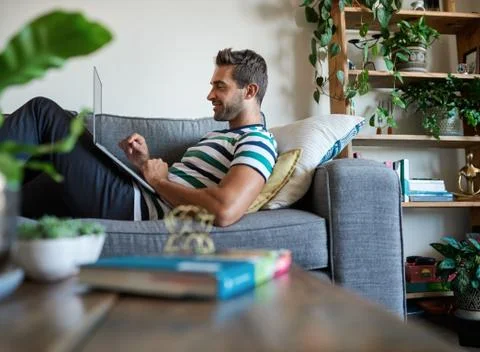 Smiling man using a laptop while sitting on his sofa Stock Photos