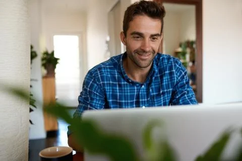 Smiling man using a laptop to work remotely from home Stock Photos
