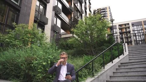 Smiling man using mobile phone and drinking coffee in the city. Slow motion Fotos Stock