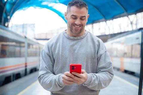 Smiling Man Using Red Smartphone at Train Station Stock Photos