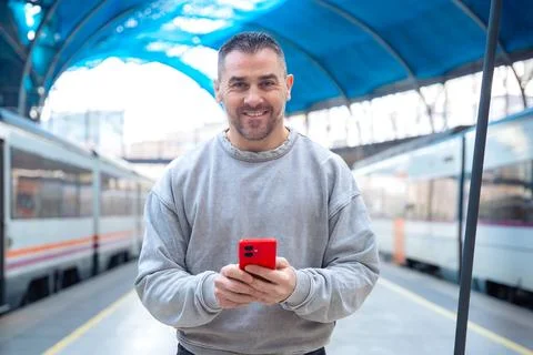Smiling Man Using Red Smartphone at Train Station looking at camera Stock Photos