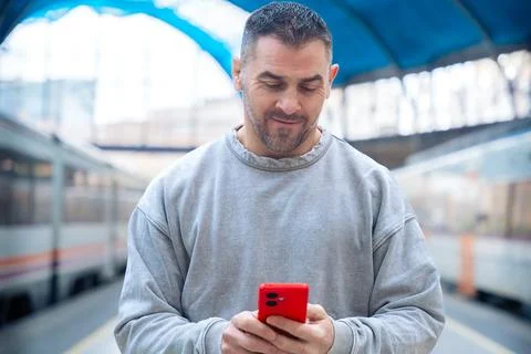 Smiling Man Using Red Smartphone at Train Station Stock Photos