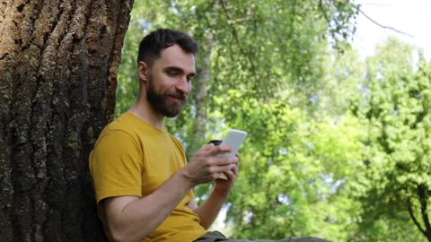 Smiling man using smartphone and drinking coffee in park 库存影片 136114590