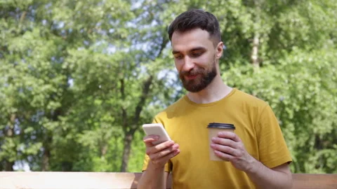 Smiling man using smartphone and drinking coffee in park Stock-Footage 136115136