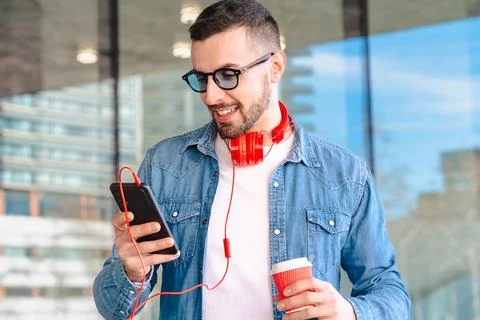 Smiling man using smartphone and holding coffee cup in modern urban setting Stock Photos