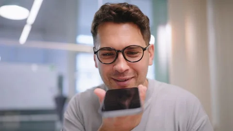 Smiling man using smartphone for online communication in modern workspace 스톡 동영상 324731173
