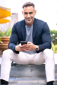 Smiling Man Using Smartphone While Sitting Outdoors in Urban Setting.Vertical Foto stock