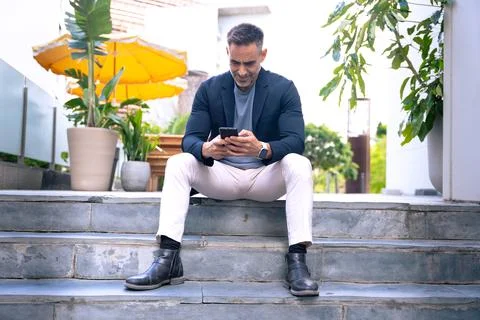 Smiling Man Using Smartphone While Sitting Outdoors in Urban Setting Stock Photos