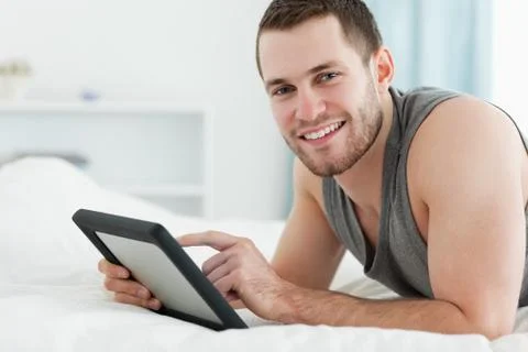 Smiling man using a tablet computer while lying on his belly Stock Photos