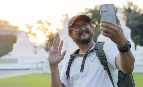Smiling man on vacation looking at smart phone and say hi with his friends. Stock Photos