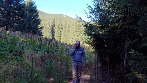 Smiling man walking along trail and talking on phone in mountains Stock Footage 344887503