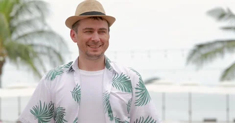 Smiling man wearing straw hat tropical shirt, beach background, summer Video stock 314045359