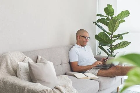 Smiling man working from home on sofa with laptop and smartphone Stock Photos